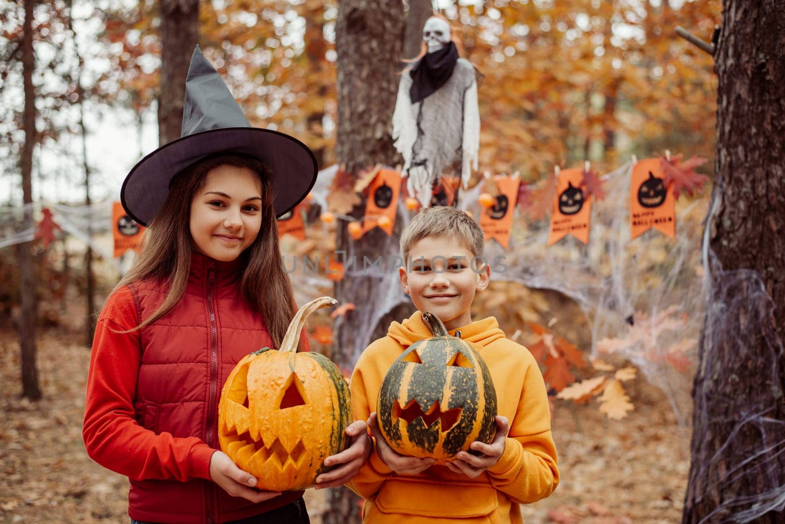 Happy boy and girl children with pumpkins in autumn forest decorated for Halloween
