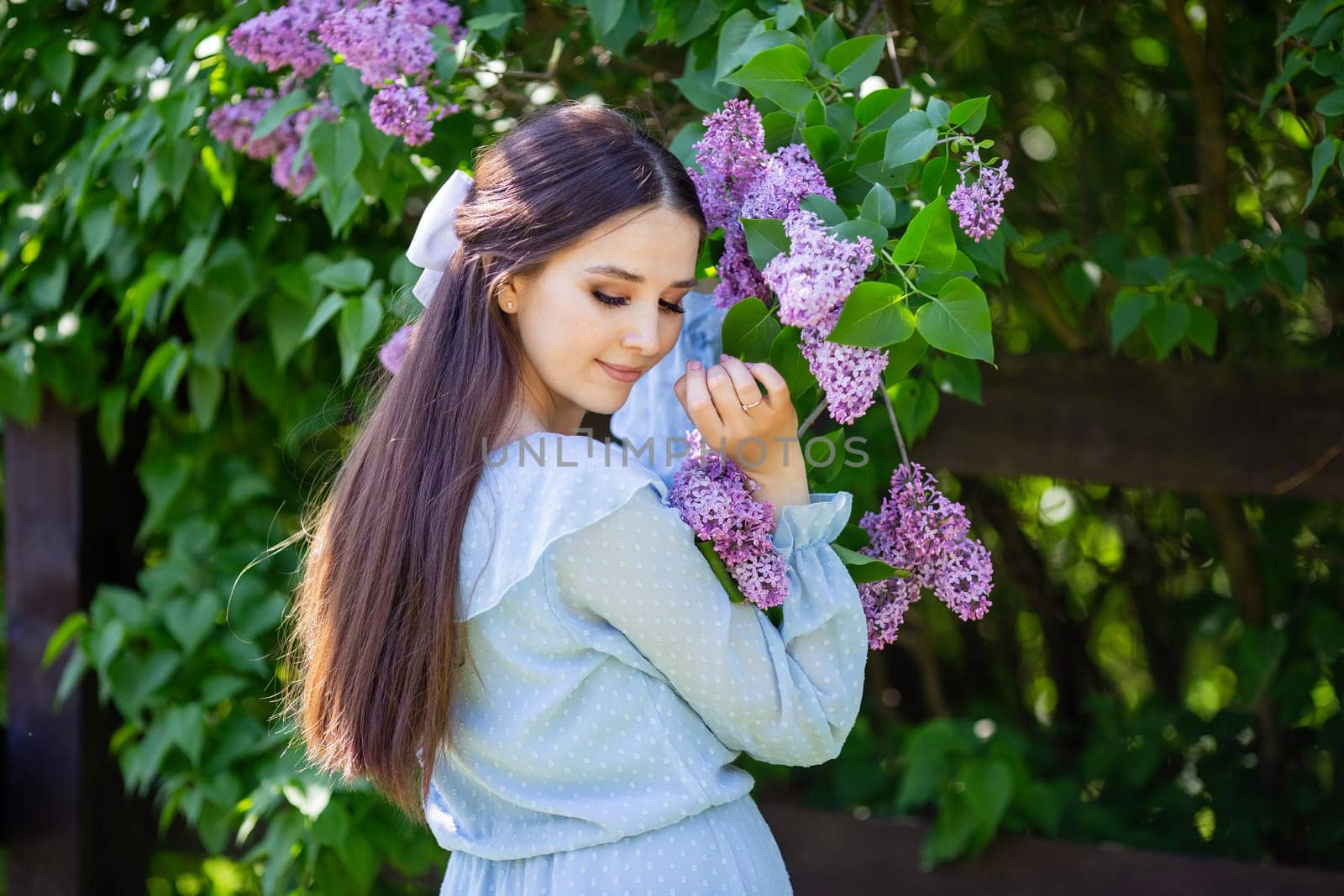 romantic girl with long hair , in light blue dress stands with lilac flowers, in the garden, in sunny day. Close up. copy space