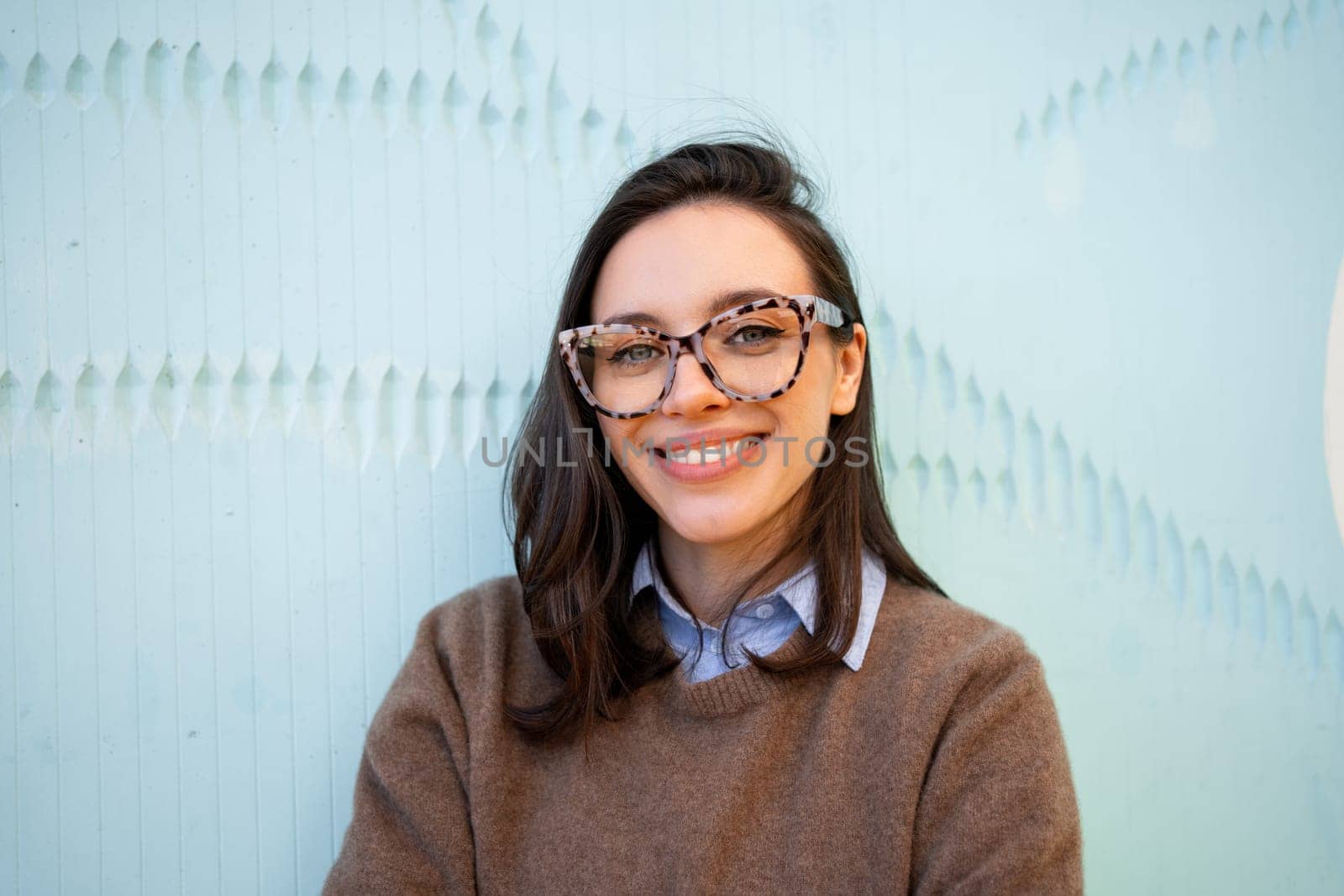Happy woman in glasses outdoor on blue color background. Positive people concept. Smiling girl in eyeglasses looking at camera. Copy space