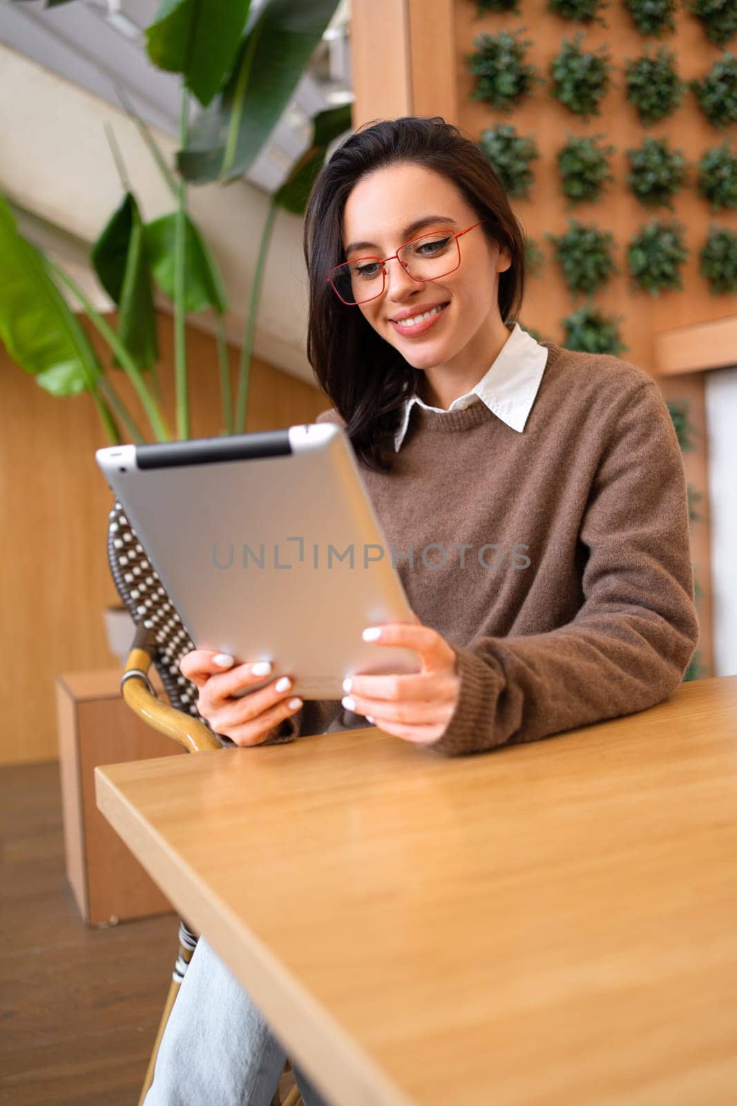 Portrait of happy woman using tablet computer sitting at her desk. Modern technologies and communication. Young female person studying or working online on touch pad looking at screen device. Vertical