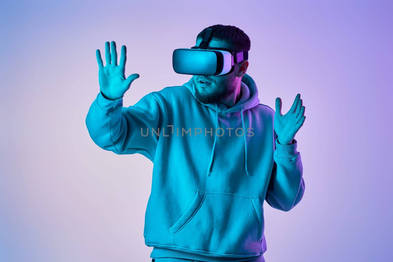 man in sweatshirt using virtual reality glasses and playing video games on blue background. Neon lighting