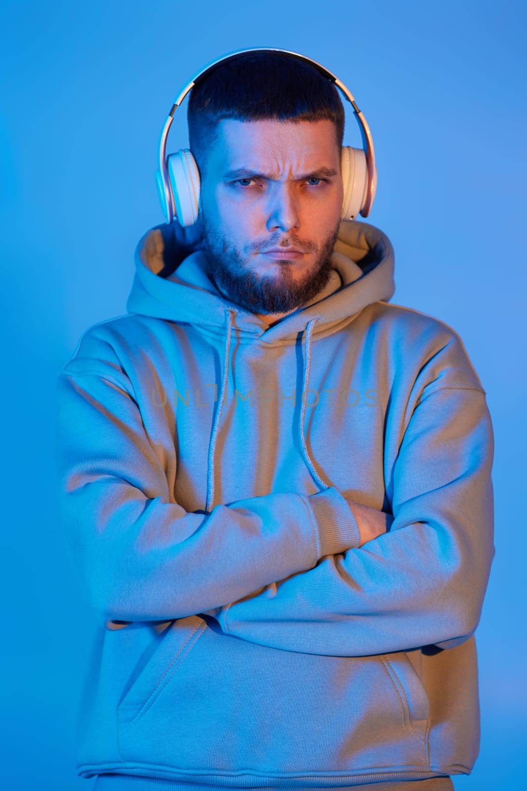 handsome bearded man with headphones in sweatshirt enjoying favorite music on blue neon background. Neon lighting