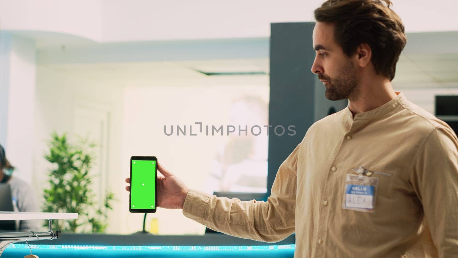 Man worker holding smartphone with greenscreen, showing blank copyspace template on mobile phone. Caucasian market assistant using isolated chroma key display in clothing store.