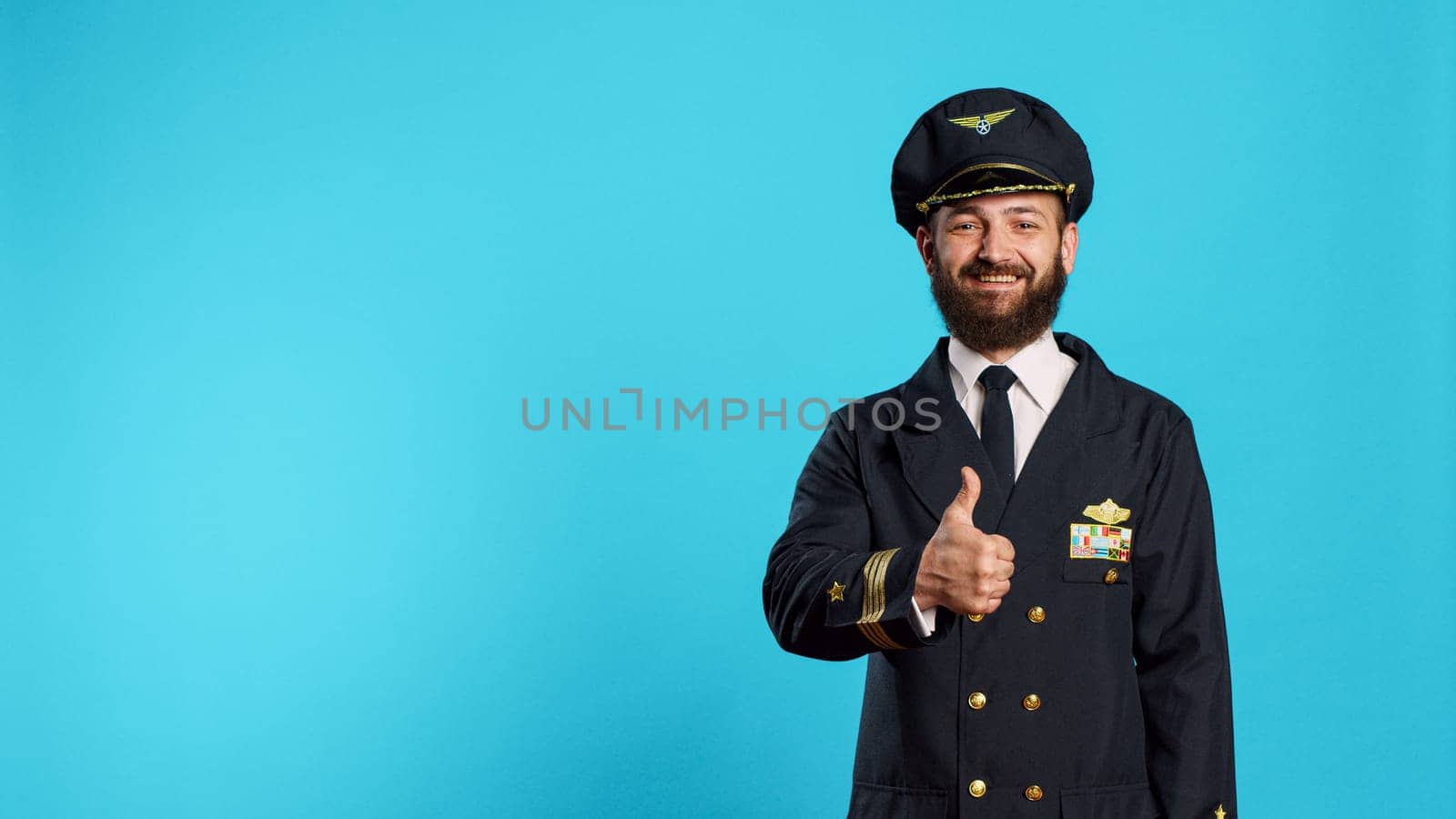 Aviation male pilot giving thumbs up on camera, expressing good sign and approval. Aircrew captain with flying uniform showing agreement and accept, doing okay symbol in studio.