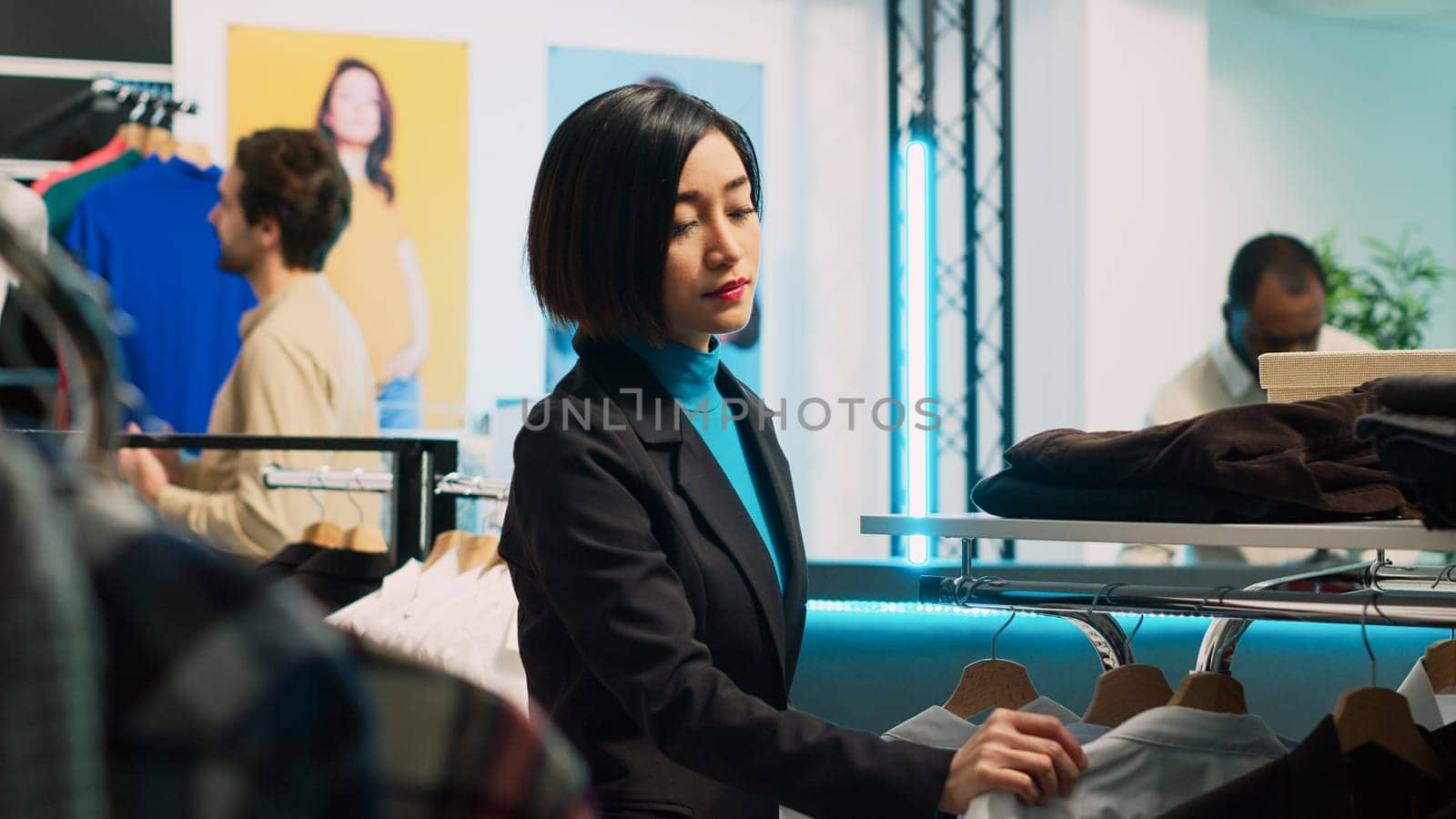 Young client shopping in fashionable boutique shop, looking at formal wear on hangers and racks. Woman buying trendy store merchandise from shopping mall, commercial activity.