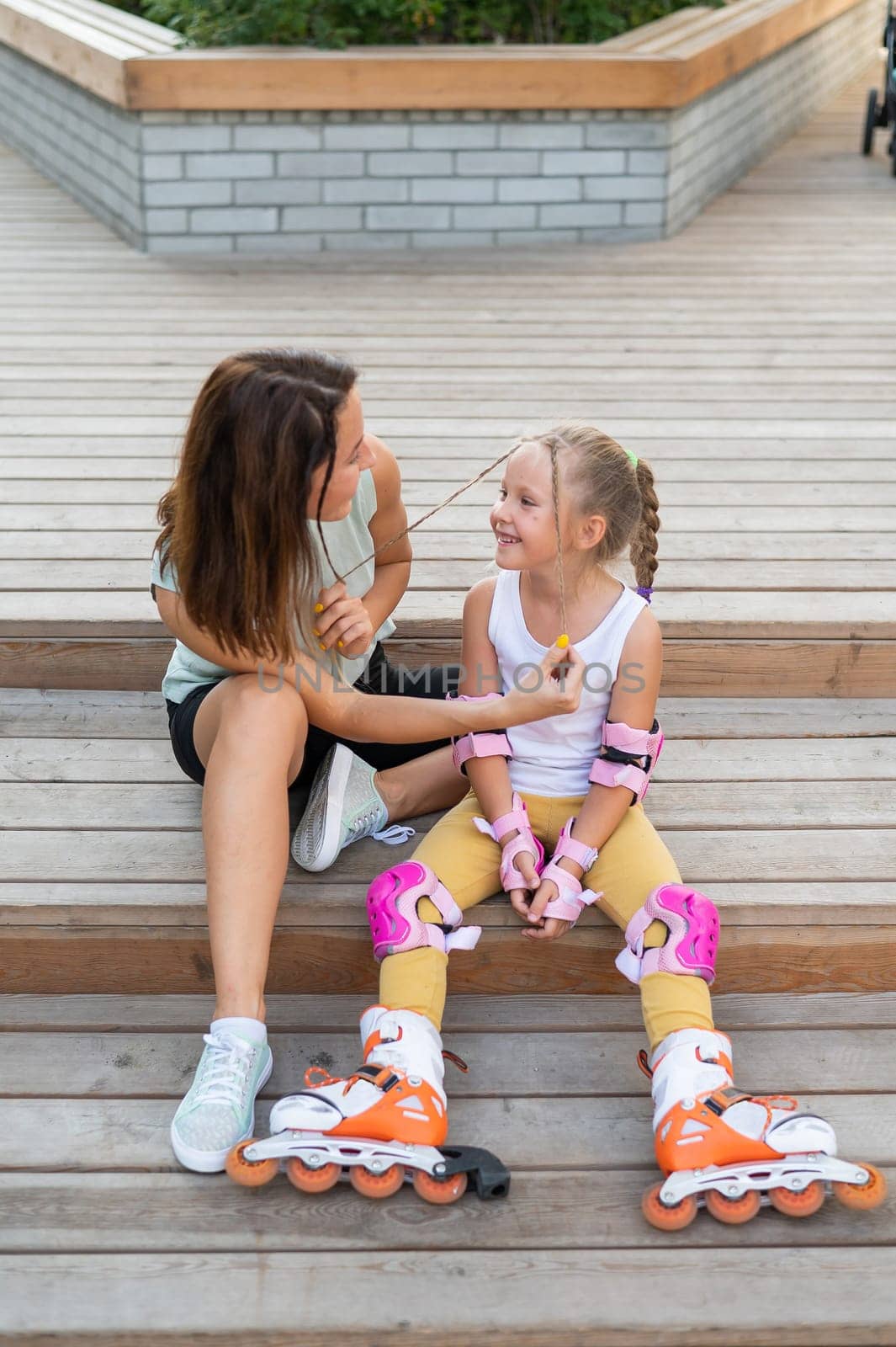 Little girl in roller skates and her mom sit on a wooden ladder and hug outdoors