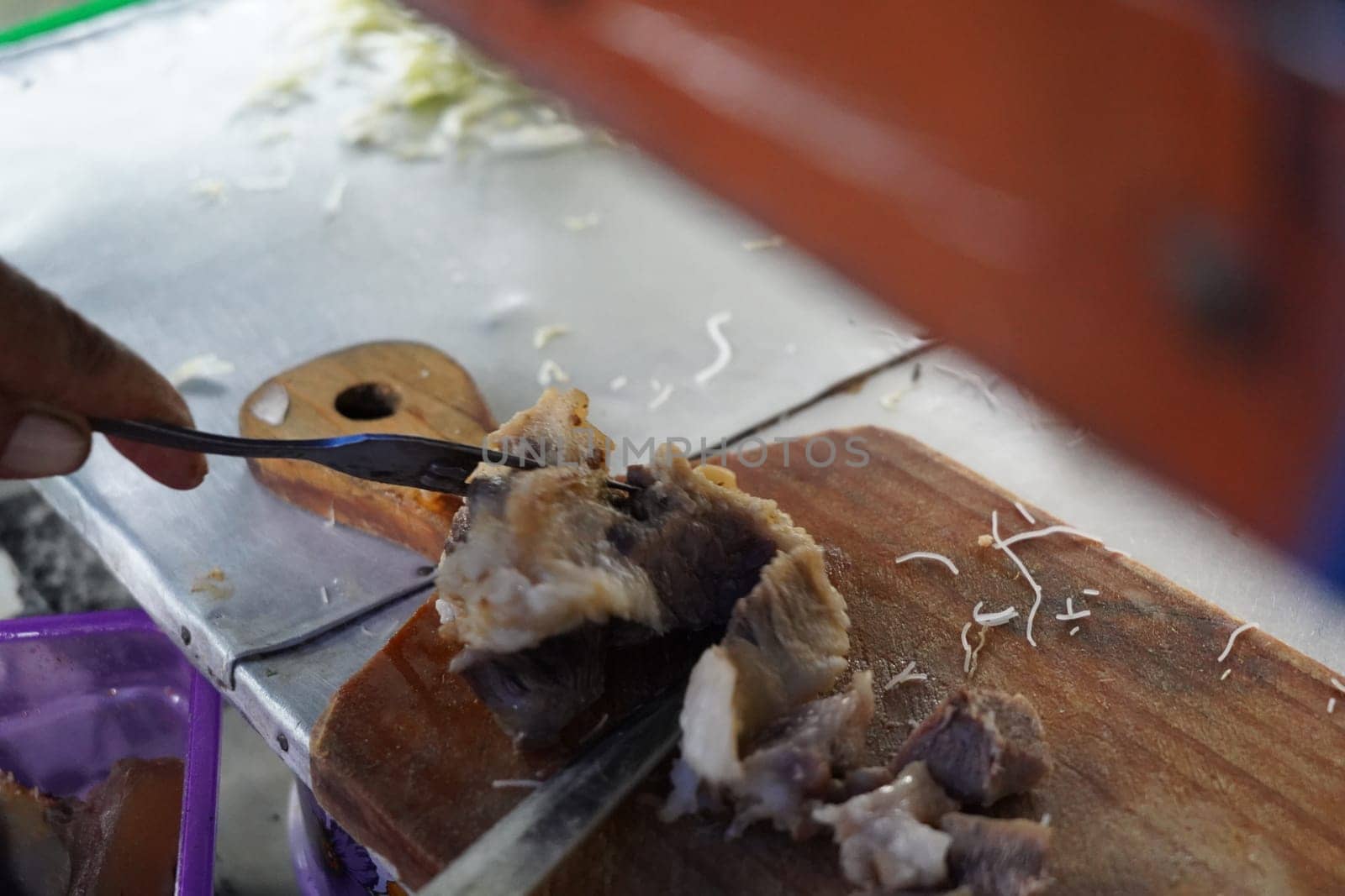 Beef brisket being chopped into bits on a wooden cutting board. Preparation for beef noodle soup in Indonesia.