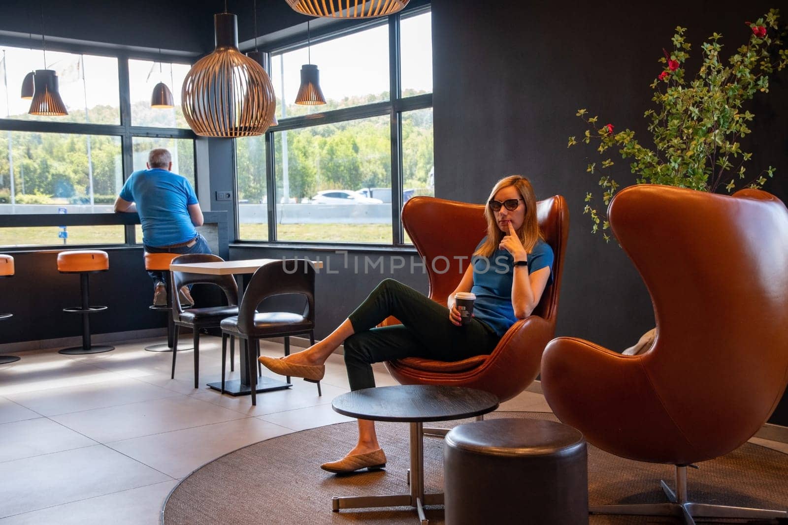 millennial blonde businesswoman sits at a table in a cafe and drinks coffee from a cardboard cup. High quality photo