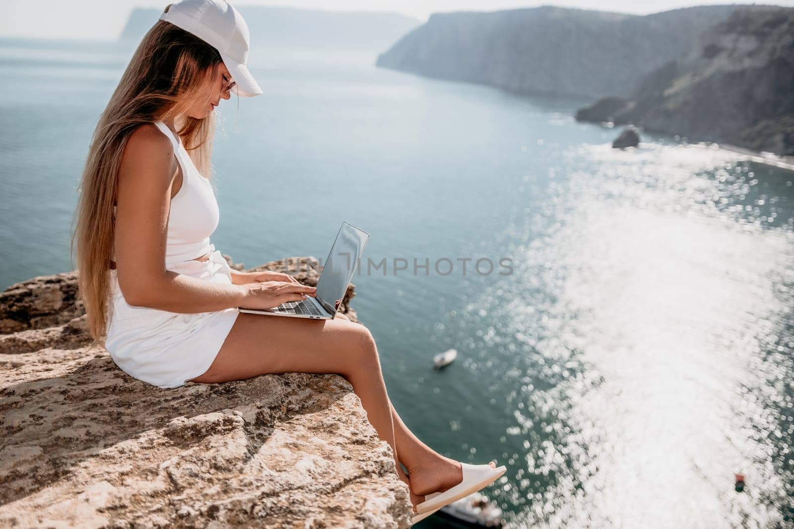 Digital nomad, Business woman working on laptop by the sea. Pretty lady typing on computer by the sea at sunset, makes a business transaction online from a distance. Freelance, remote work on vacation by panophotograph