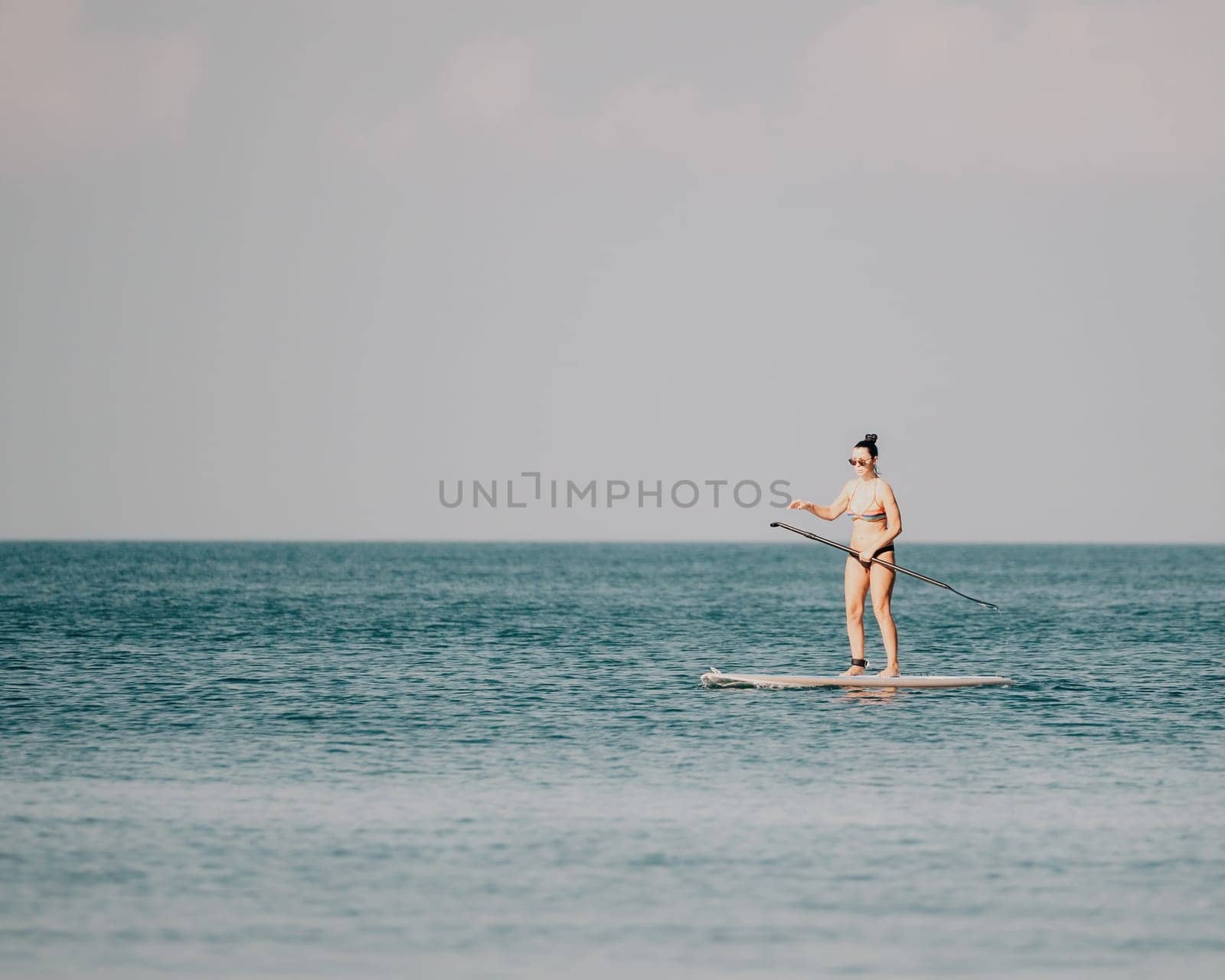 Sea woman sup. Silhouette of happy middle aged woman in rainbow bikini, surfing on SUP board, confident paddling through water surface. Idyllic sunset. Active lifestyle at sea or river