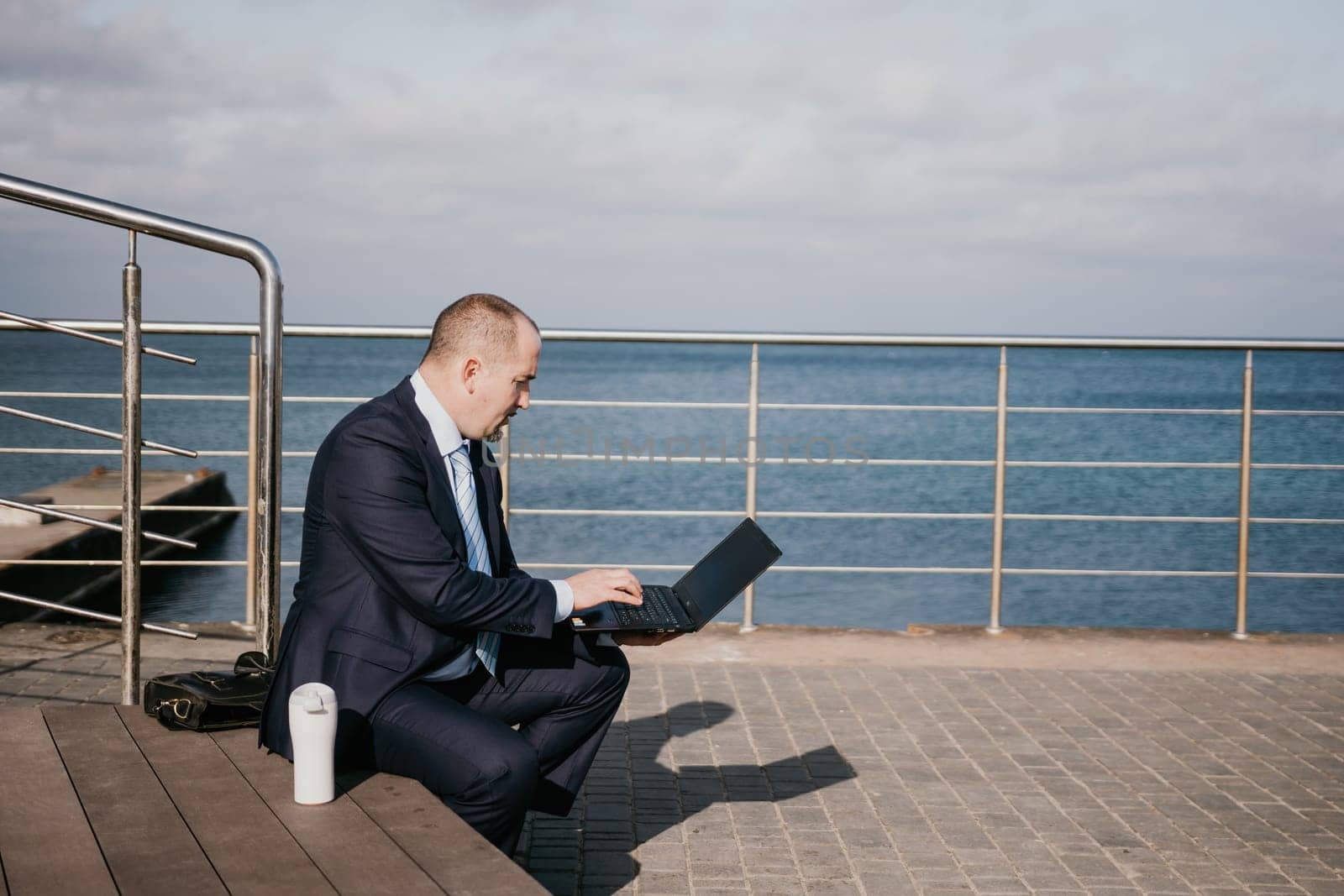 Digital Nomad, a young tattooed man working remotely online, typing on a laptop keyboard while sitting on a beach at sunset. Working remotely on vacation, running an online business from a distance
