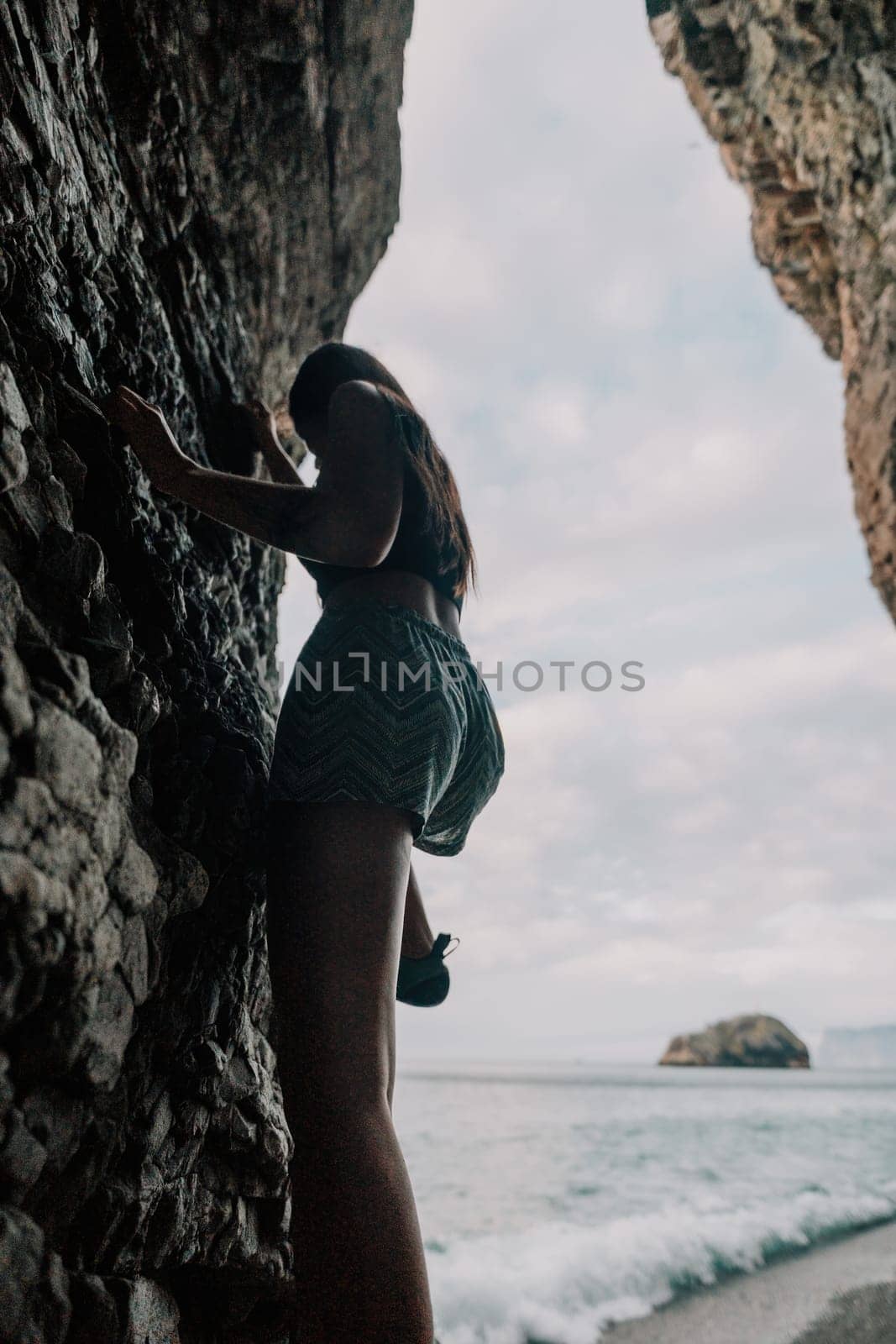 A girl climbs a rock. The athlete trains in nature. Woman overcomes difficult climbing route. Extreme hobby. Tourist woman rock climber hiking on mountains rocks over beautiful sea coast
