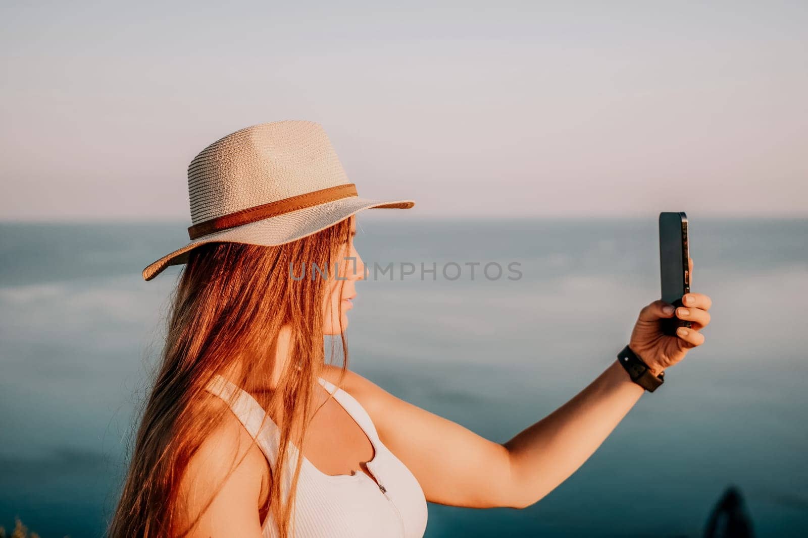 Woman travel sea. Happy tourist in hat enjoy taking picture outdoors for memories. Woman traveler posing on the beach at sea surrounded by volcanic mountains, sharing travel adventure journey. by panophotograph