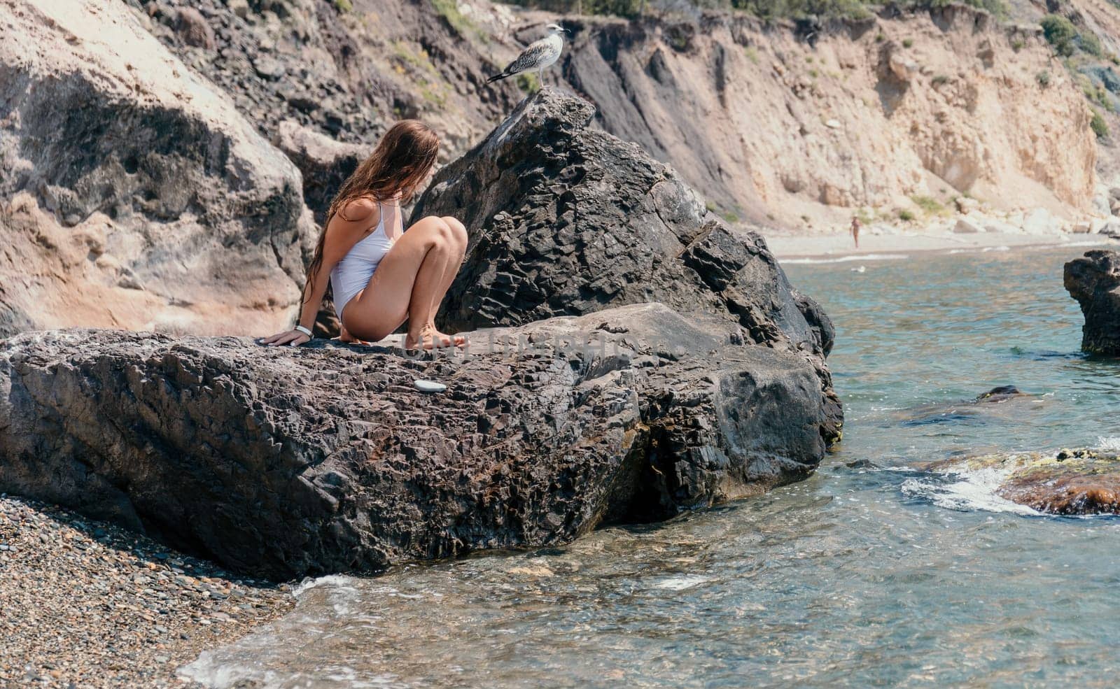 Woman travel sea. Young Happy woman in a long red dress posing on a beach near the sea on background of volcanic rocks, like in Iceland, sharing travel adventure journey