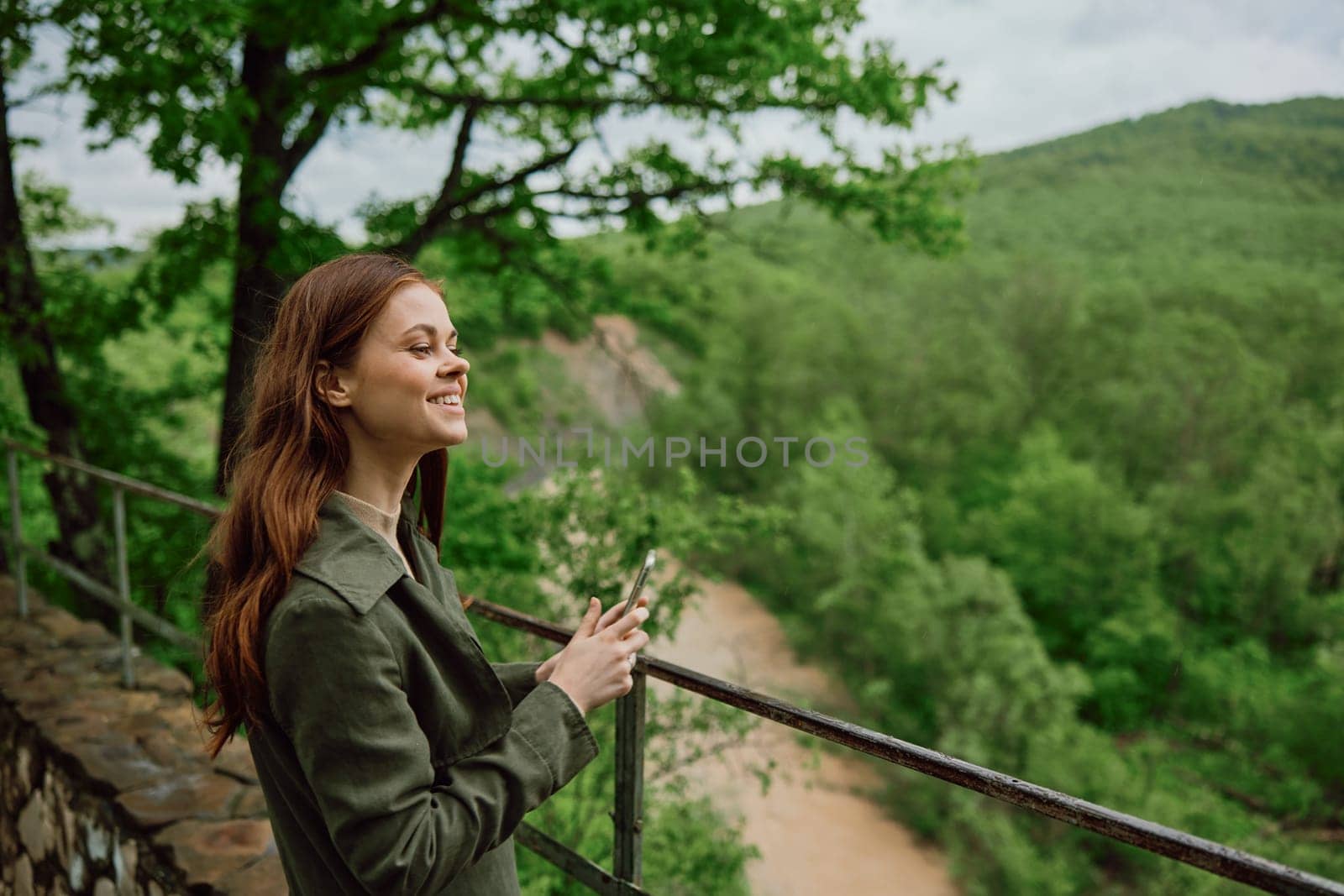 a woman in a raincoat takes pictures on the phone of a beautiful view of the forest. Travel, technology, mobile photography. High quality photo