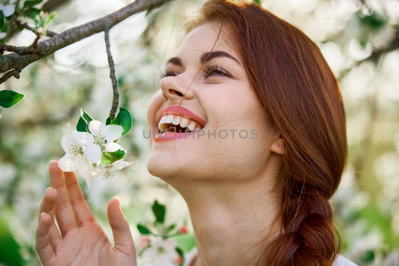 close portrait of a red-haired, laughing woman smelling flowers from a tree. High quality photo