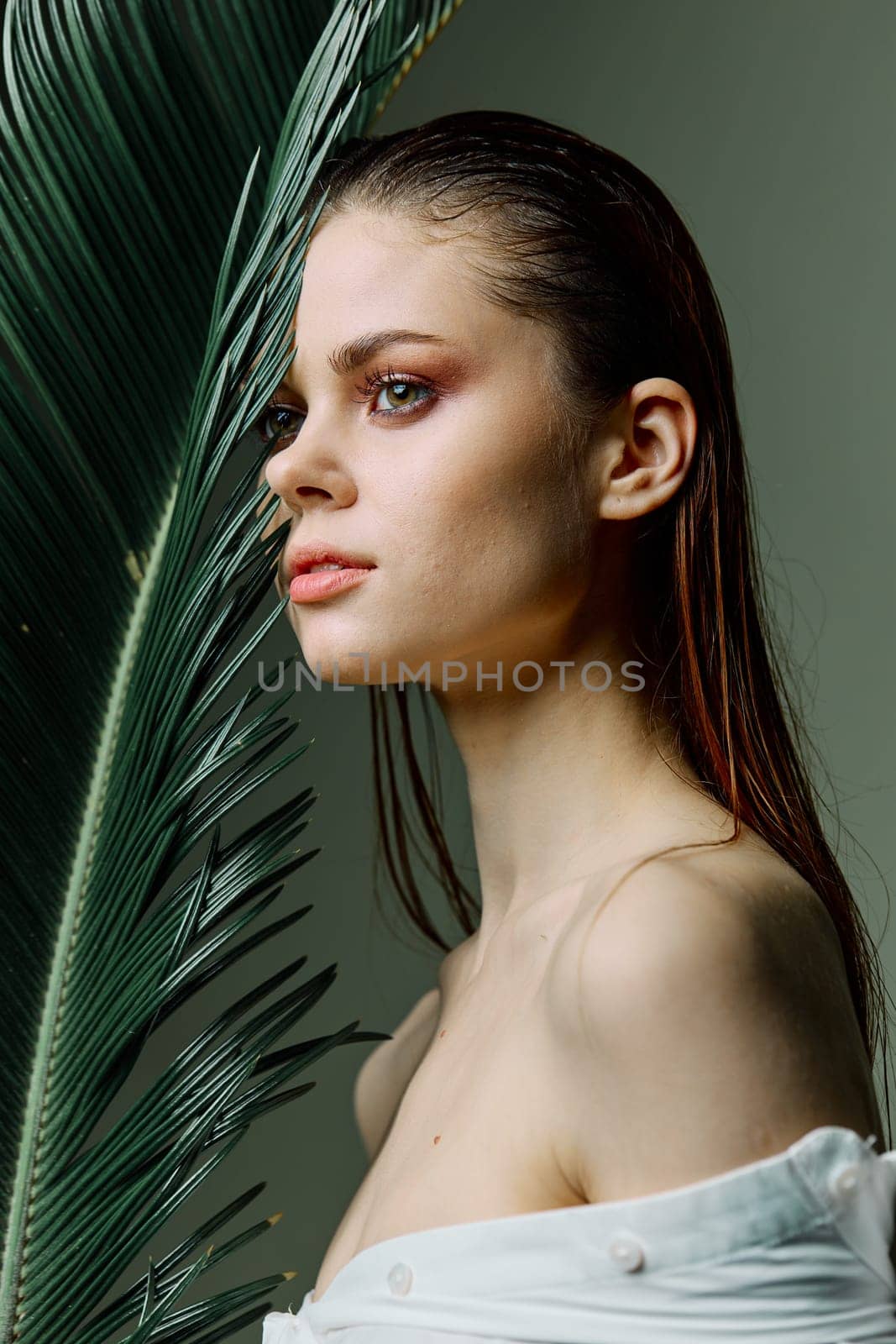 vertical photo portrait of an elegant woman with her hair slicked back, standing with a palm leaf holding it near her face. High quality photo