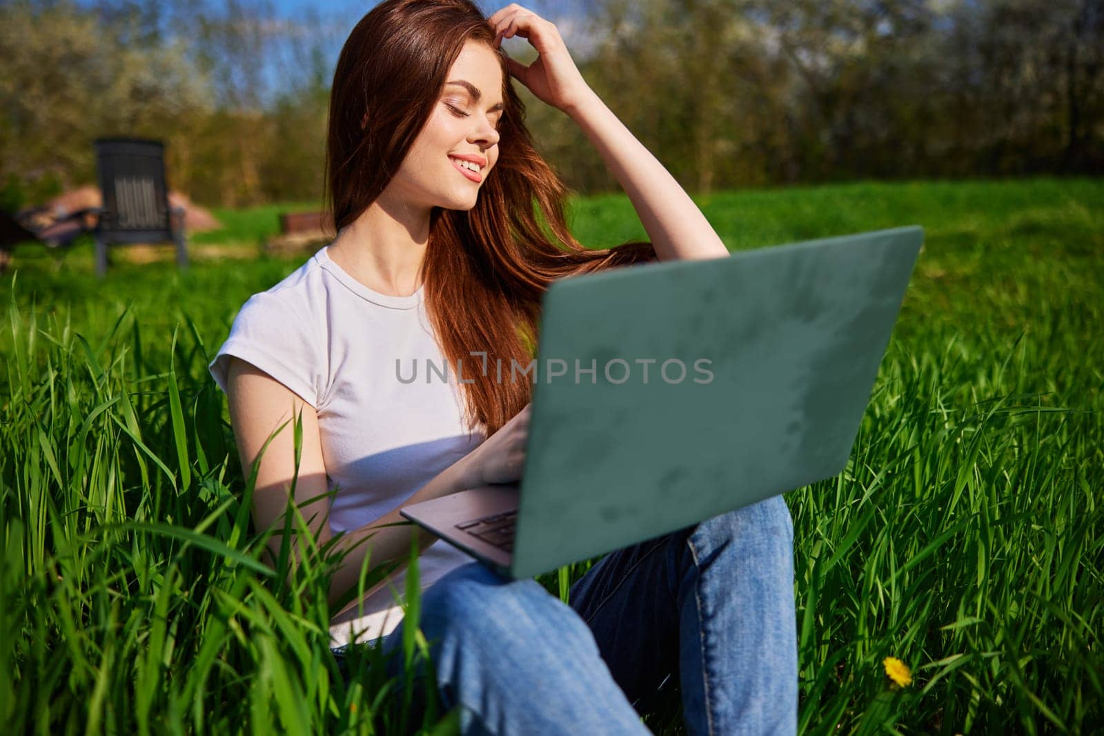 happy, joyful woman working on a laptop while sitting in a field by Vichizh