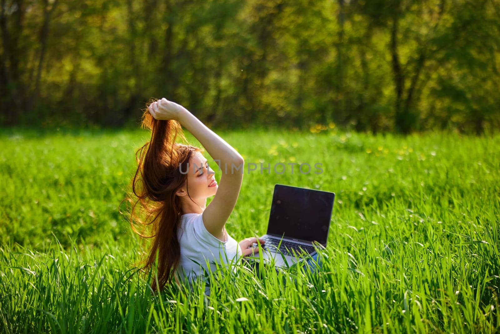 woman working at a laptop sitting in a field straightens her hair by Vichizh