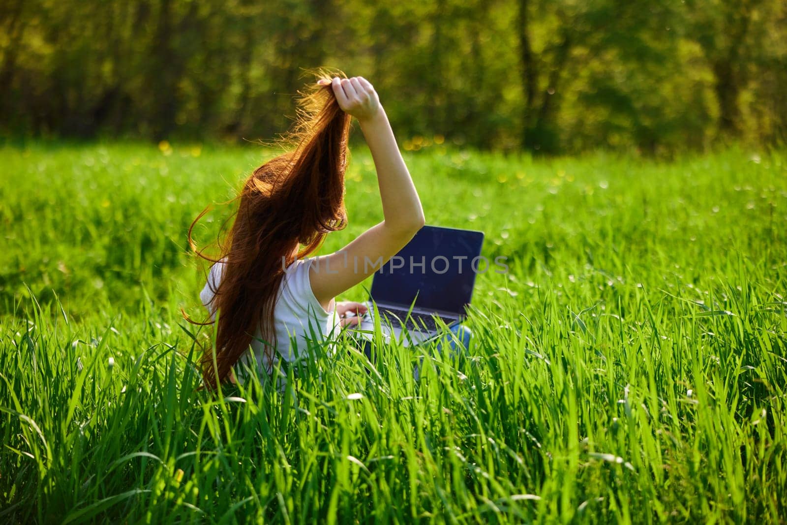 woman working at a laptop sitting in a field straightens her hair by Vichizh