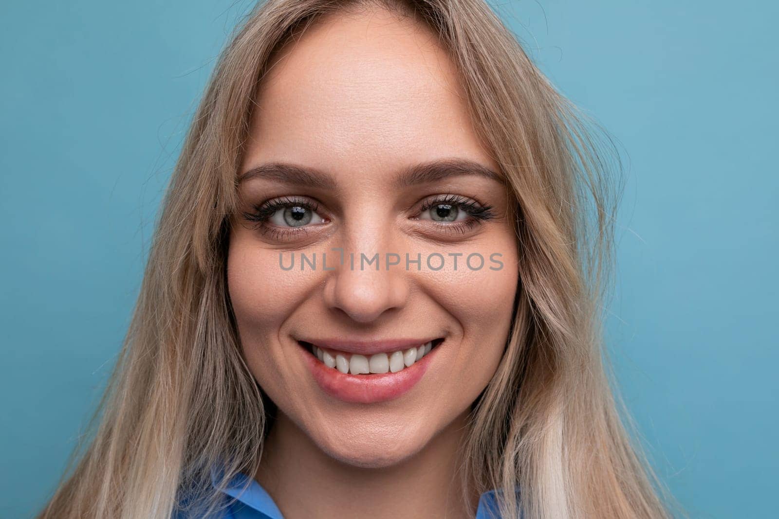 beautiful young woman in a blue shirt smiling cheerfully on a blue background.