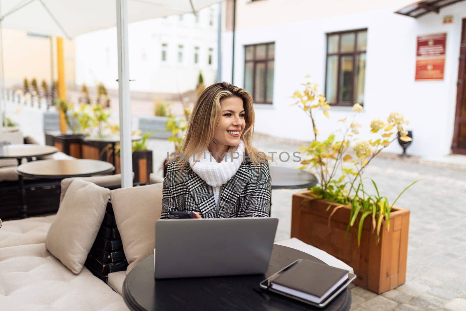 young european woman model in street cafe with laptop in spring.