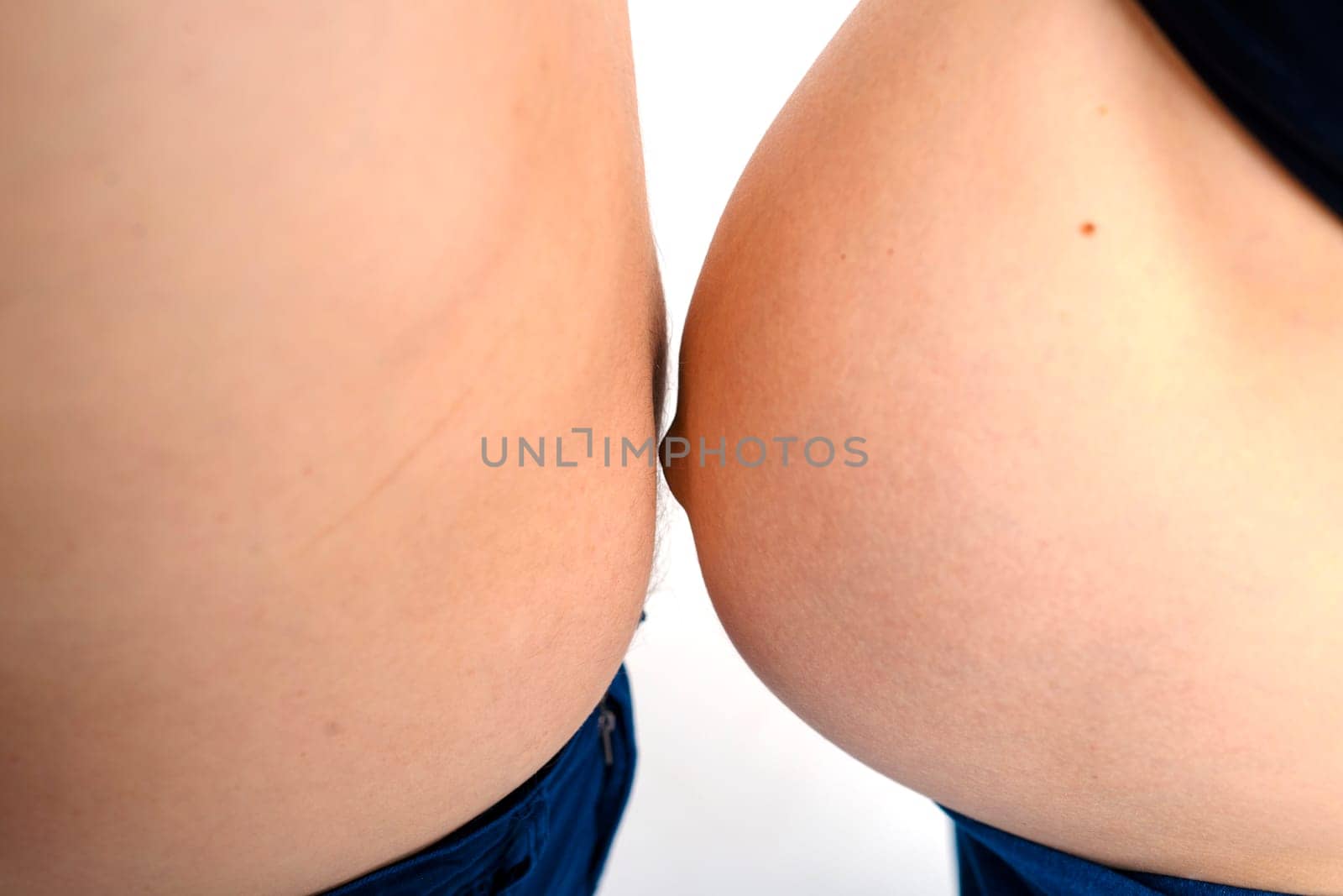 the pregnant belly of the wife and the fat belly of the husband are measured in size. a young couple of expectant parents compares the thickness of the abdomen