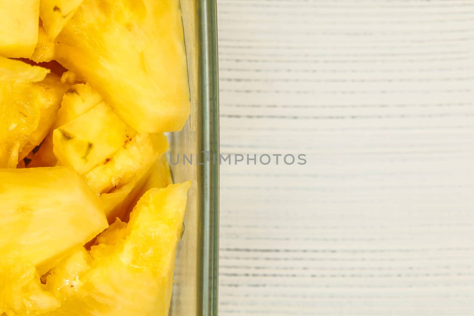 Tabletop view, detail - yellow pineapple cut in pieces, in square glass bowl, white boards desk / space for text on right.