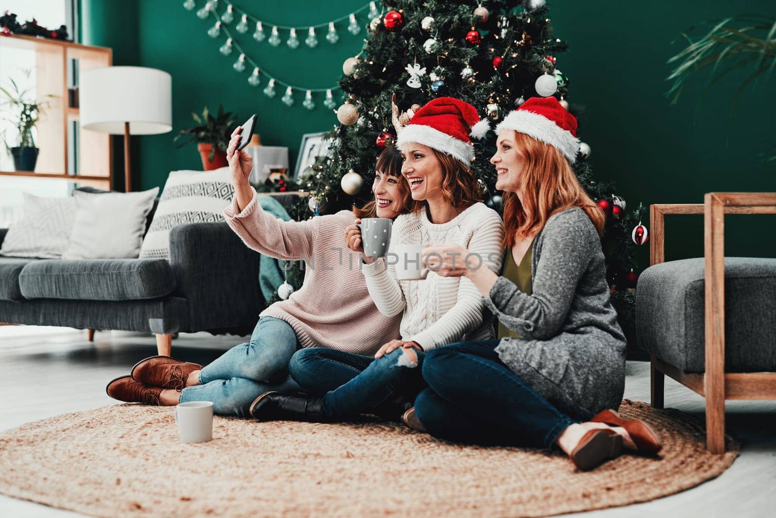 Capturing memories. three attractive middle aged women taking self portraits together with a cellphone at home during Christmas time