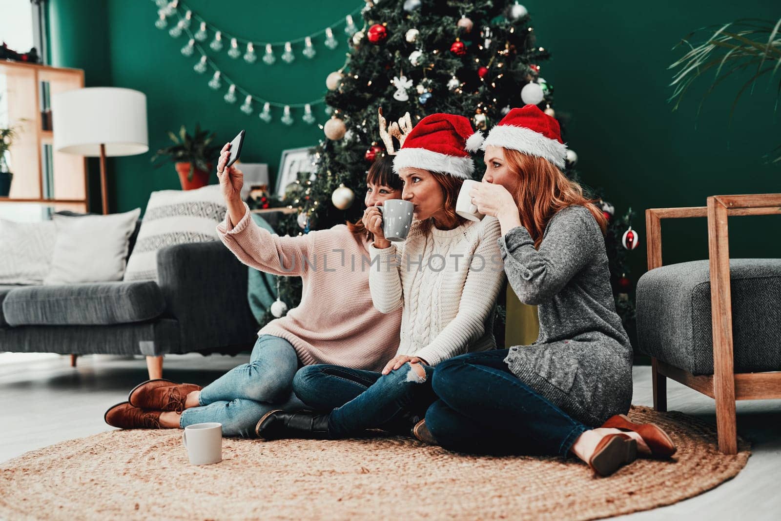 Arent we just looking festive. three attractive middle aged women taking self portraits together with a cellphone at home during Christmas time