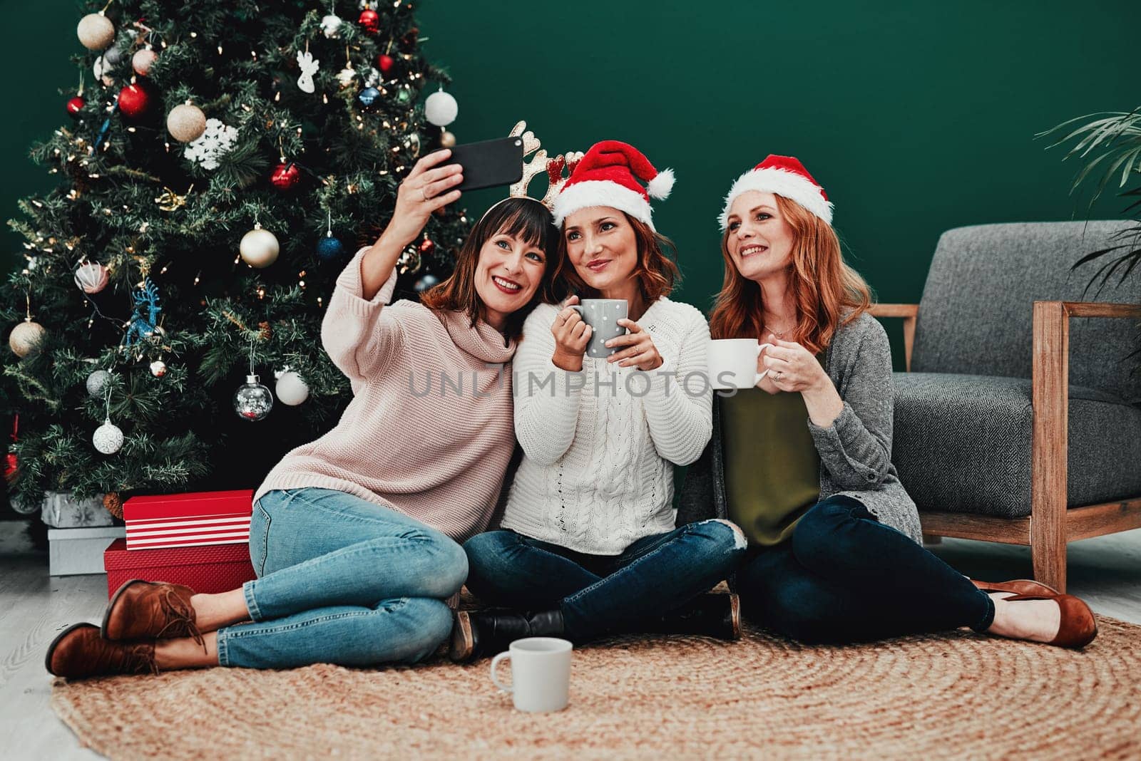 This photo is going to come out great. three attractive middle aged women taking self portraits together with a cellphone at home during Christmas time