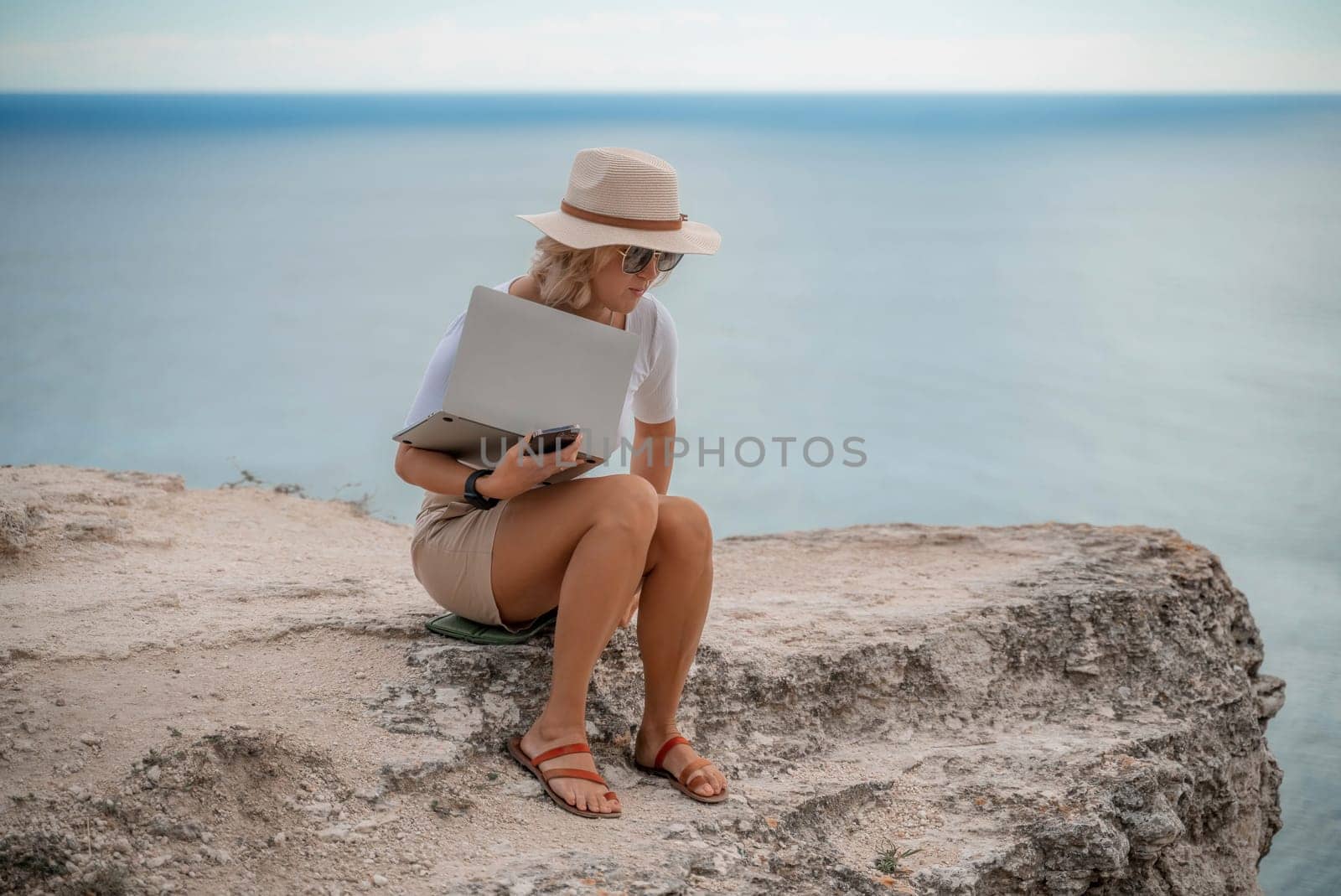 Freelance women sea working on the computer. Good looking middle aged woman typing on a laptop keyboard outdoors with a beautiful sea view. The concept of remote work