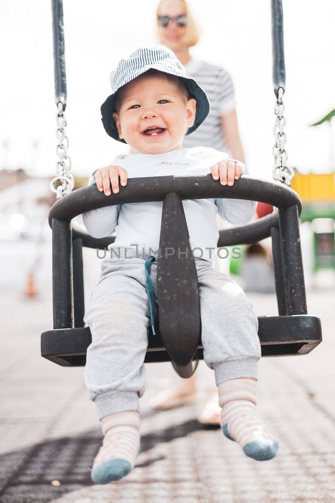 Mother pushing her infant baby boy child on a swing on playground outdoors