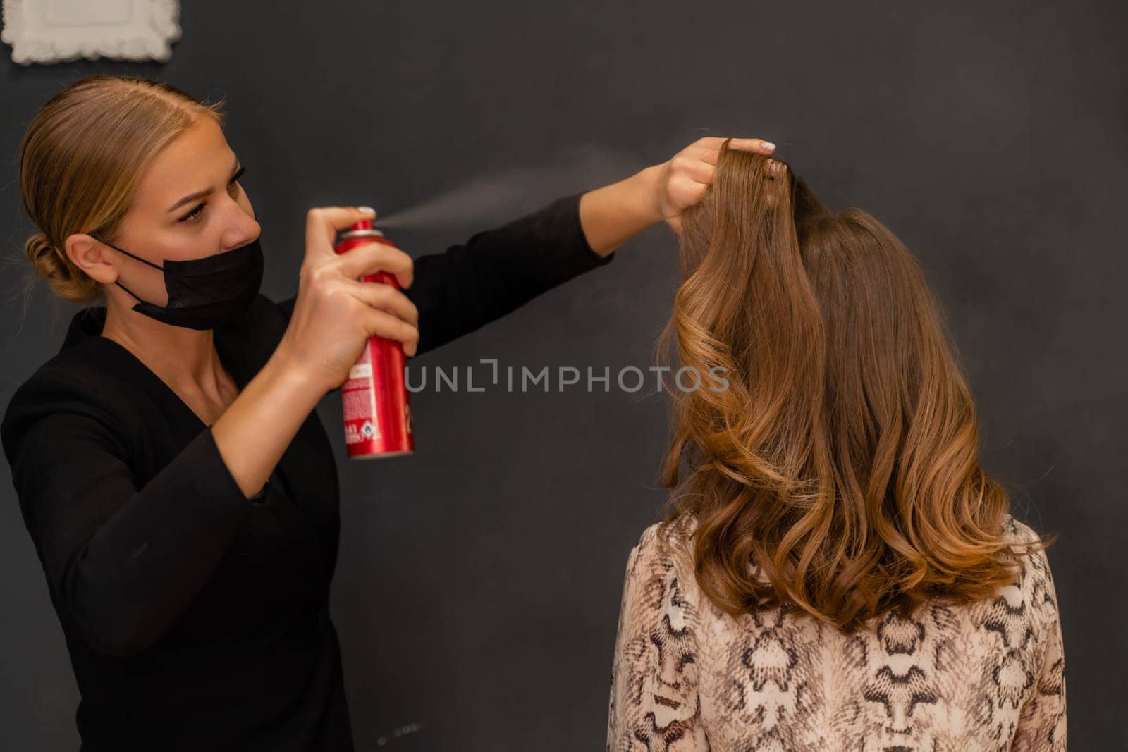 Women salon hairstyle. Hairdresser uses hairspray on client's hair in salon, Portrait of two beautiful women.