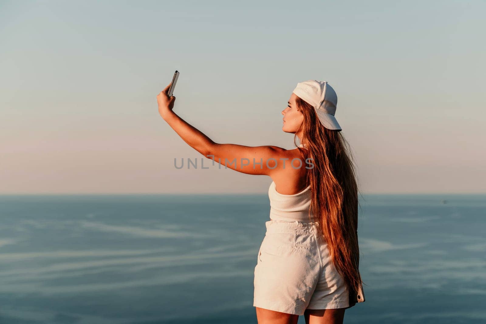 Selfie woman in a cap, white tank top and shorts makes a selfie shot mobile phone post photo social network outdoors on the background of the sea beach people vacation lifestyle travel concept