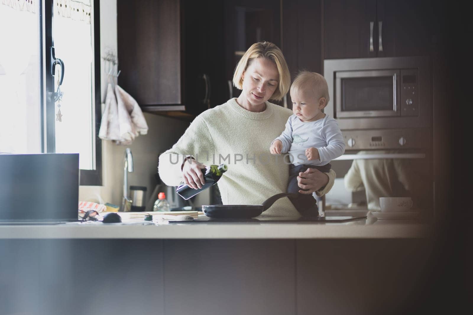 Happy mother and little infant baby boy together making pancakes for breakfast in domestic kitchen. Family, lifestyle, domestic life, food, healthy eating and people concept. by kasto