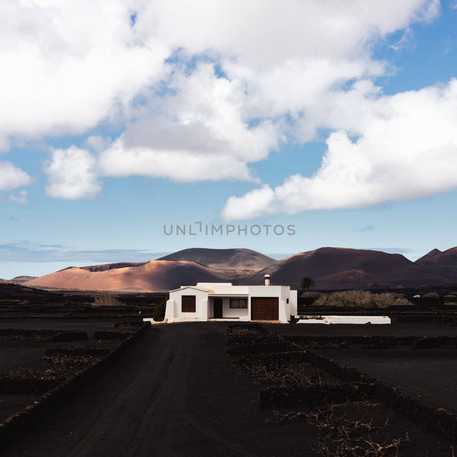 Traditional white house in black volcanic landscape of La Geria wine growing region with view of Timanfaya National Park in Lanzarote. Touristic attraction in Lanzarote island, Canary Islands, Spain. by kasto