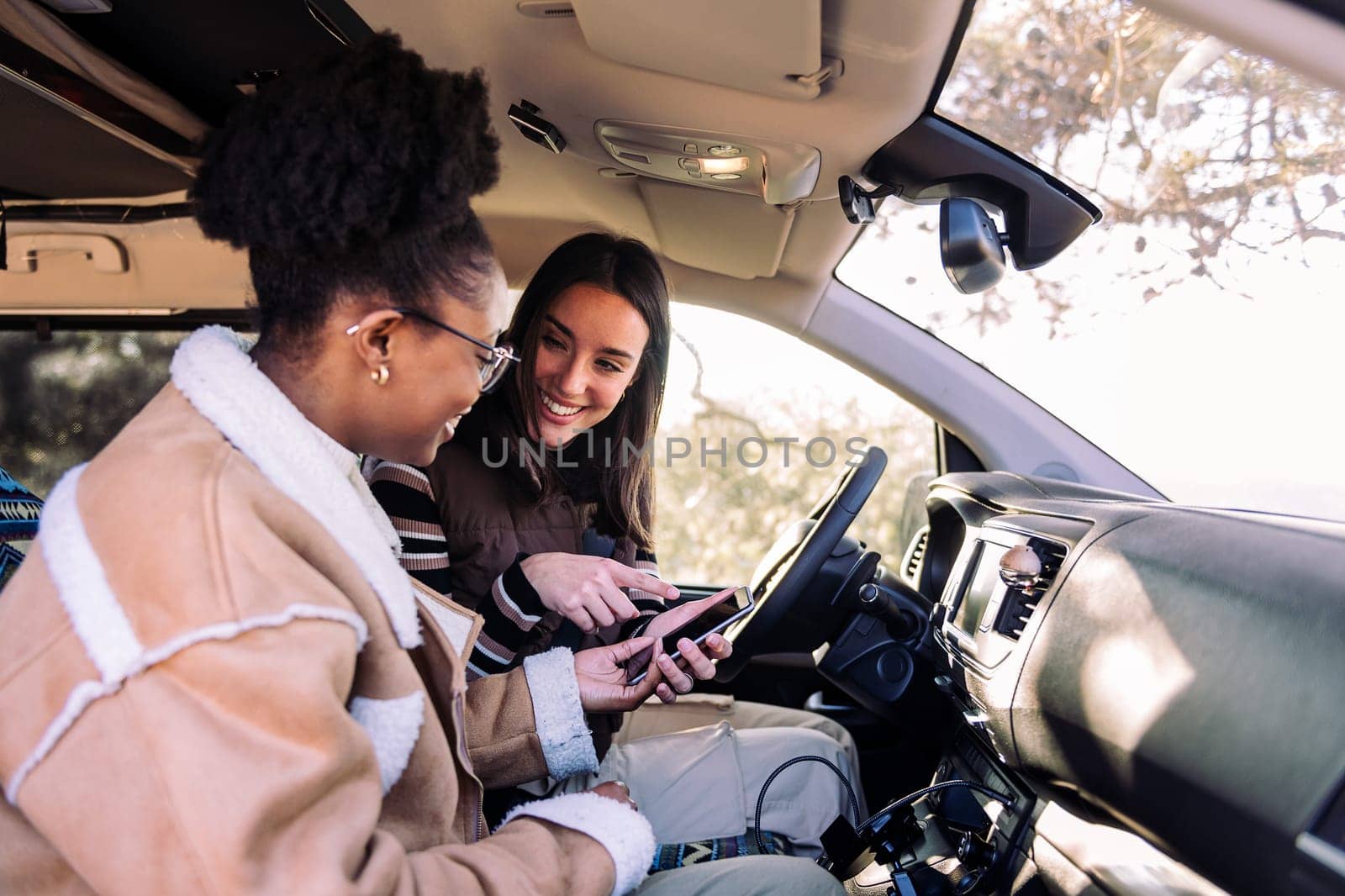Two young women on the road in camper van using navigation app on the mobile phone, concept of adventure and travel with best friend