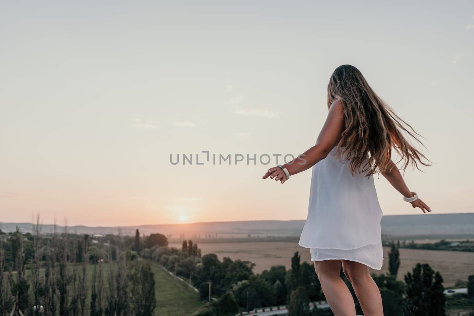 Romantic beautiful bride in white dress posing with sea and mountains in background. Stylish bride standing back on beautiful landscape of sea and mountains on sunset