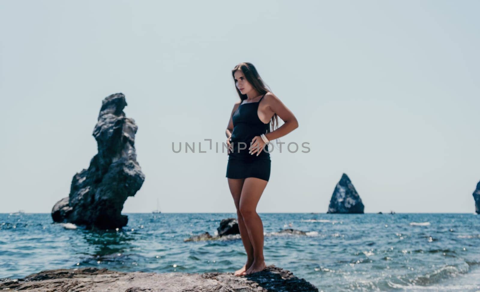 Woman travel sea. Young Happy woman in a long red dress posing on a beach near the sea on background of volcanic rocks, like in Iceland, sharing travel adventure journey