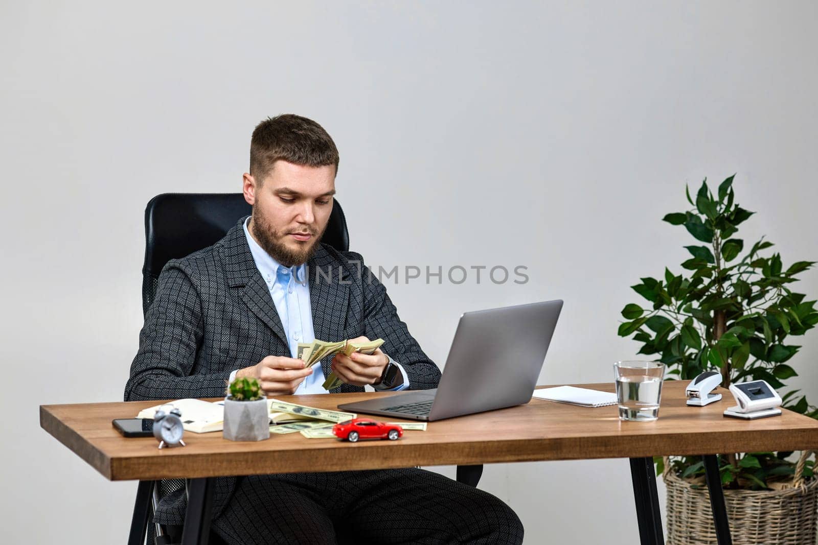 young bearded businessman works on laptop and counts money at office desk