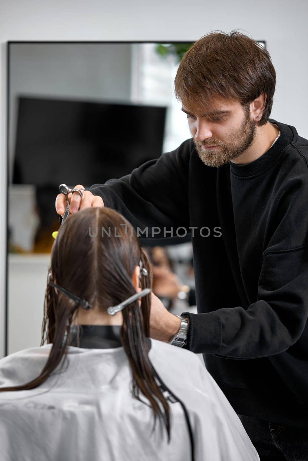 Professional male hairdresser with scissors cutting female hair in salon