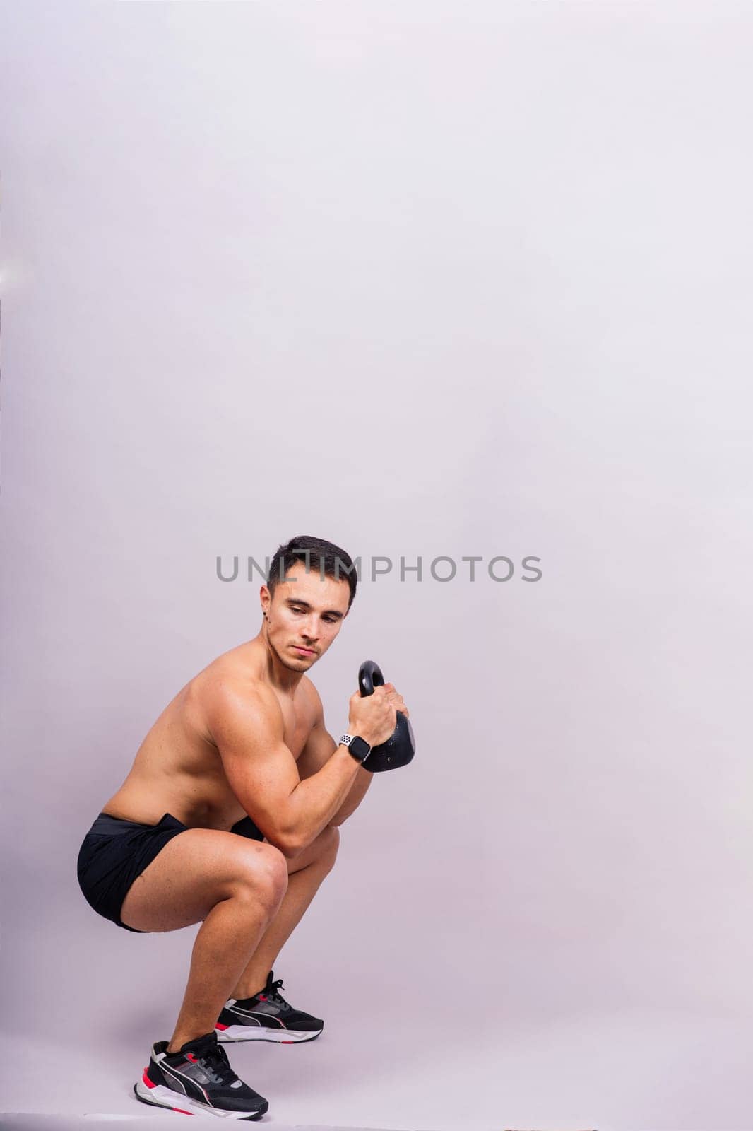 Strong young muscular focused fit man with big muscles holding heavy kettlebells by Zelenin