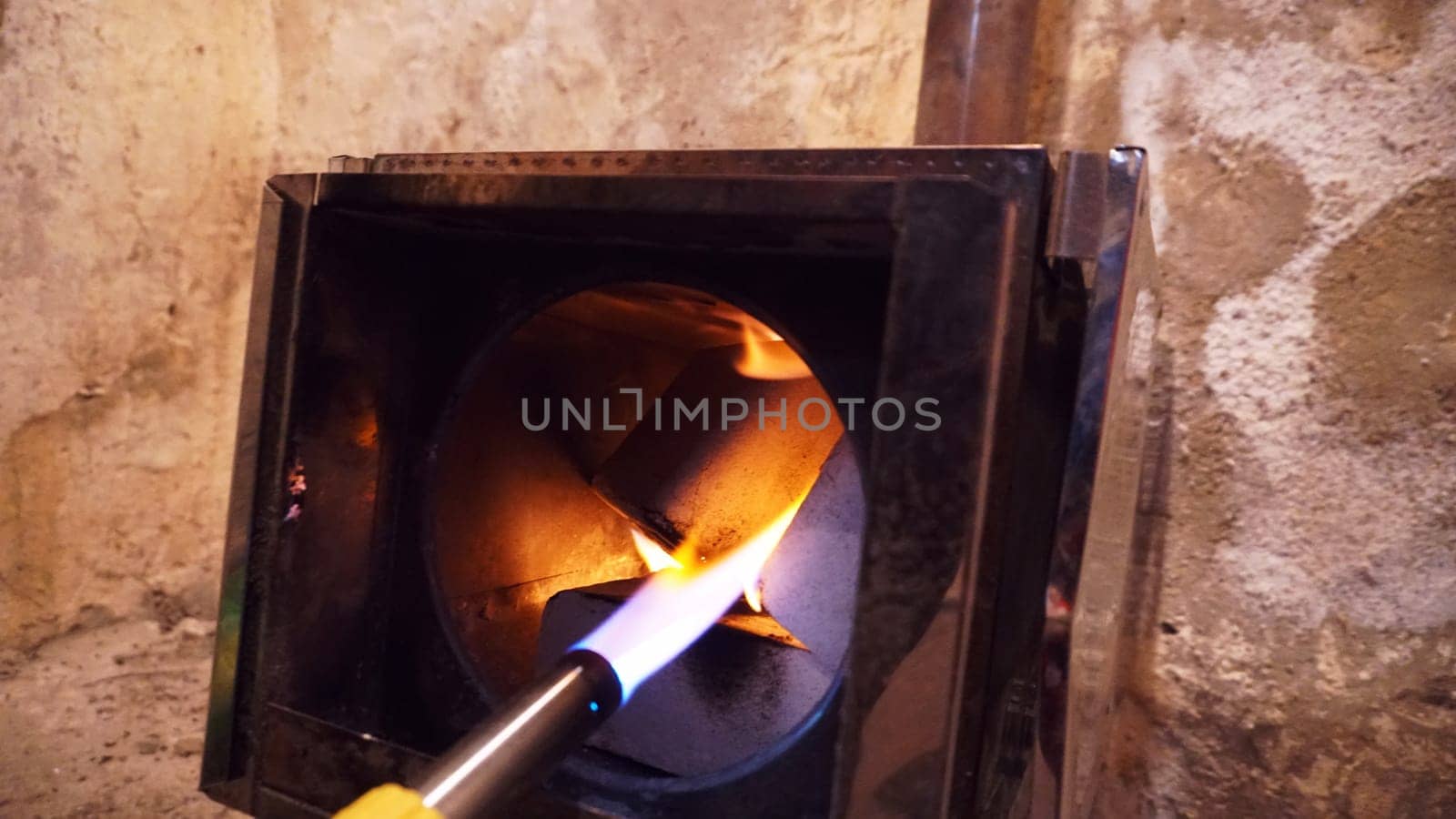 The guy lights a fire in the oven. To lay firewood. Camping stove with fuel briquettes. We make a fire with a gas burner. A smoke extraction hole is visible. The shiny walls of the furnace.