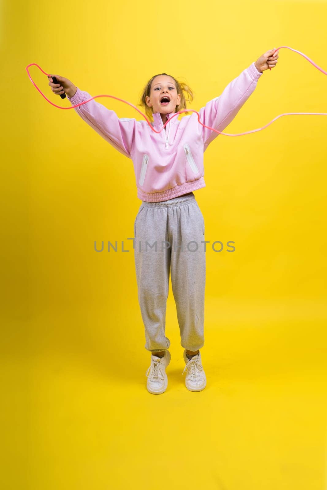 Adorable female child with skipping rope jumping in studio by Zelenin