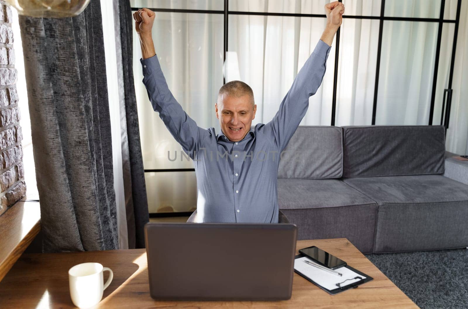 A businessman working at a computer rejoices in a perfect successful transaction, raising his hands up. The concept of success.