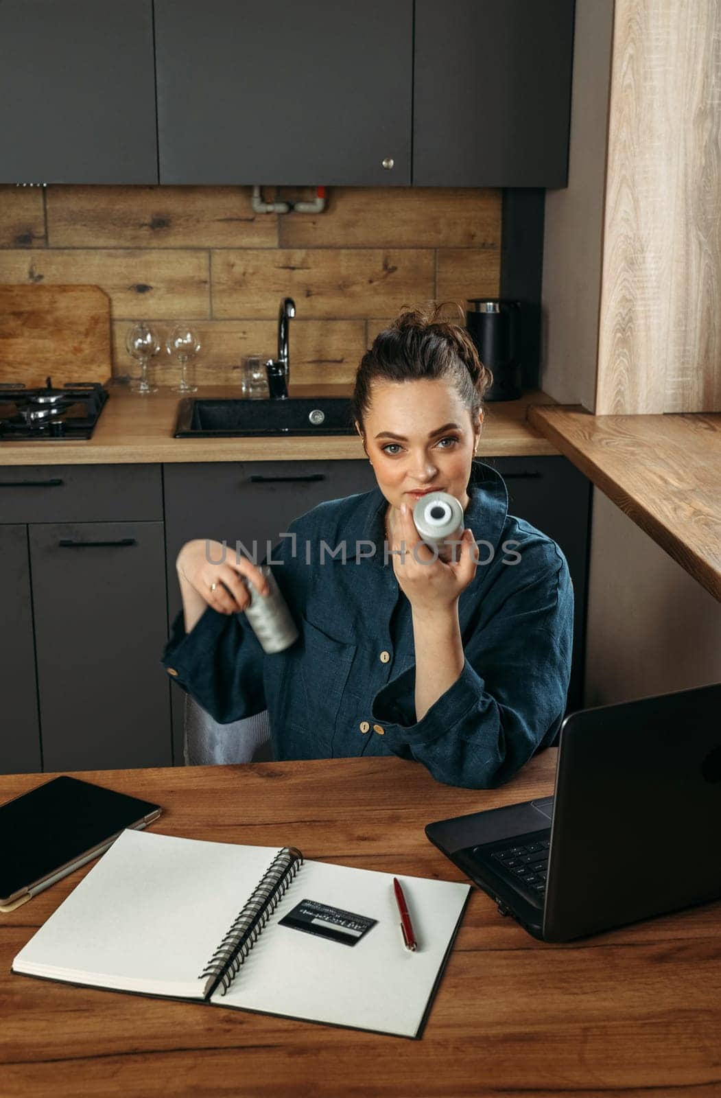 Portrait of a beautiful cheerful female clothing stylist who sits at a table near a laptop and looks through large spools of thread. Vertical frame.