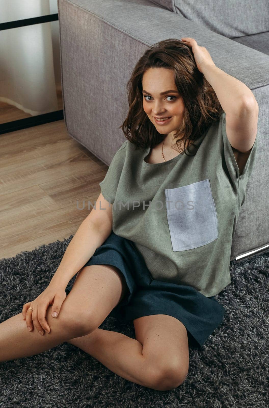 Portrait of a beautiful woman who sits indoors on the floor, straightens her hair. View from above.