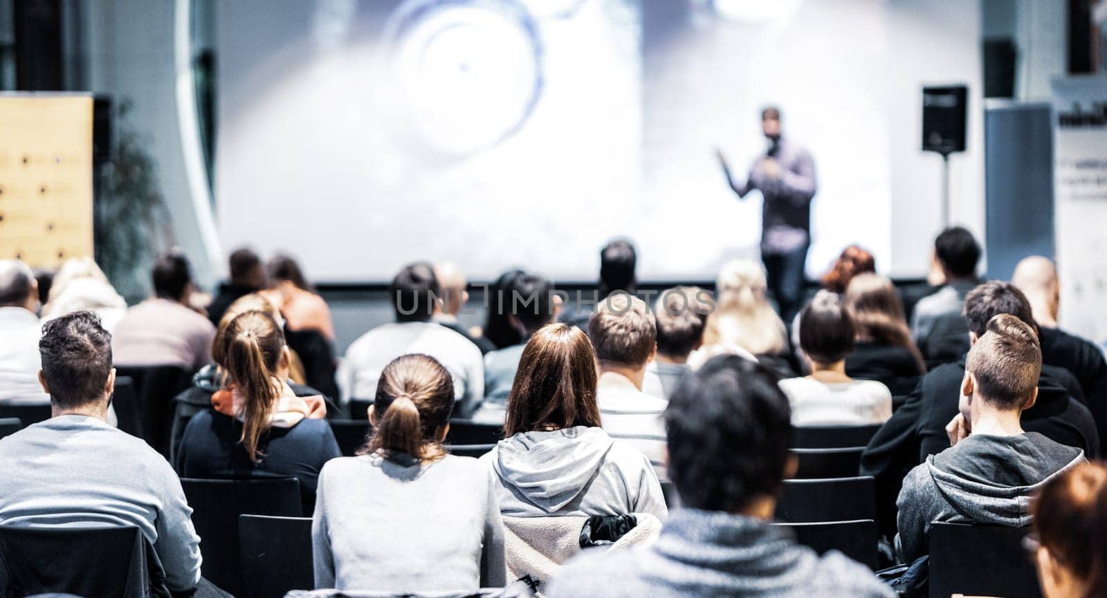 Speaker giving a talk in conference hall at business event. Rear view of unrecognizable people in audience at the conference hall. Business and entrepreneurship concept.