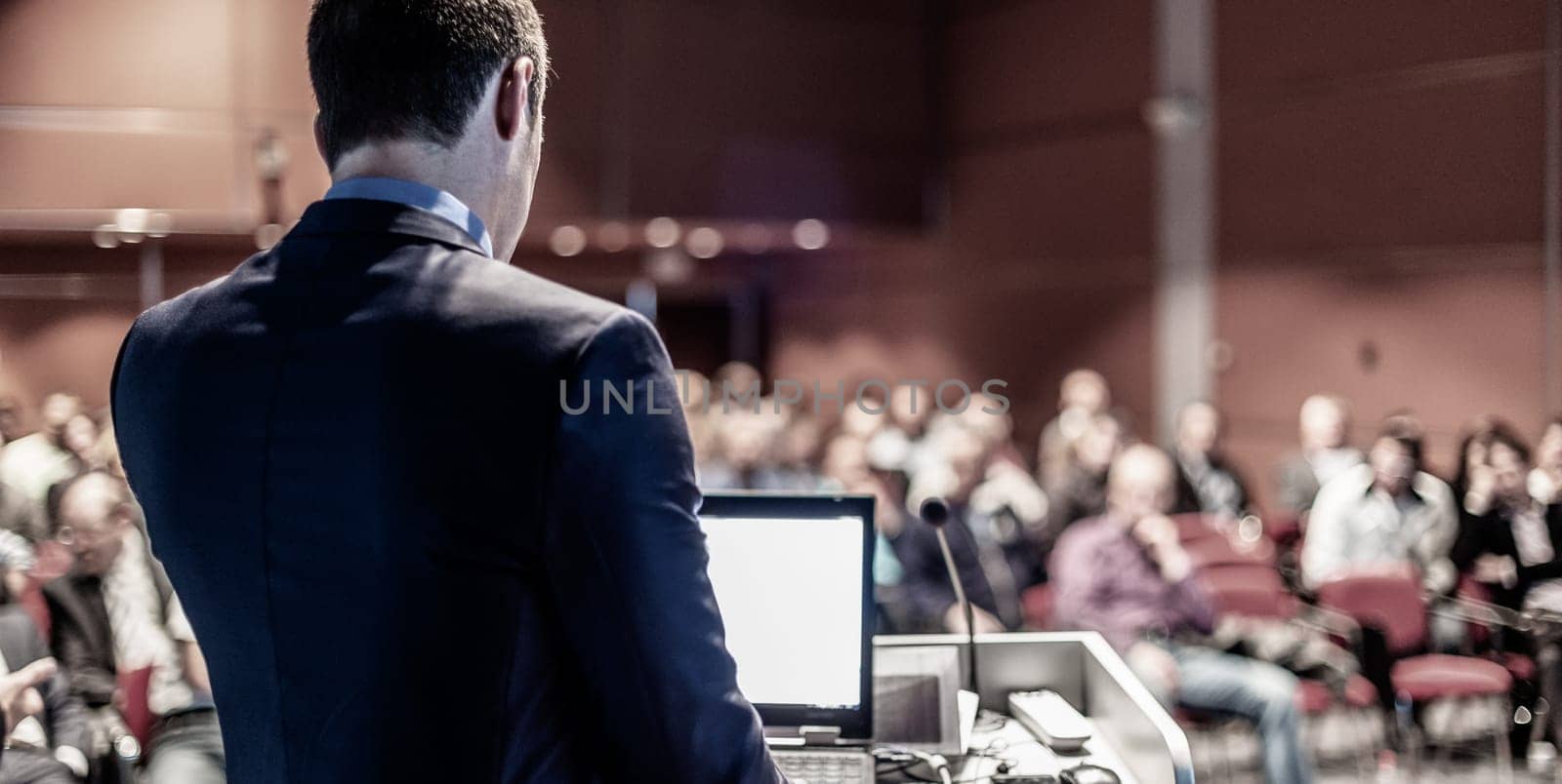 Speaker giving a talk on corporate business conference. Unrecognizable people in audience at conference hall. Business and Entrepreneurship event.